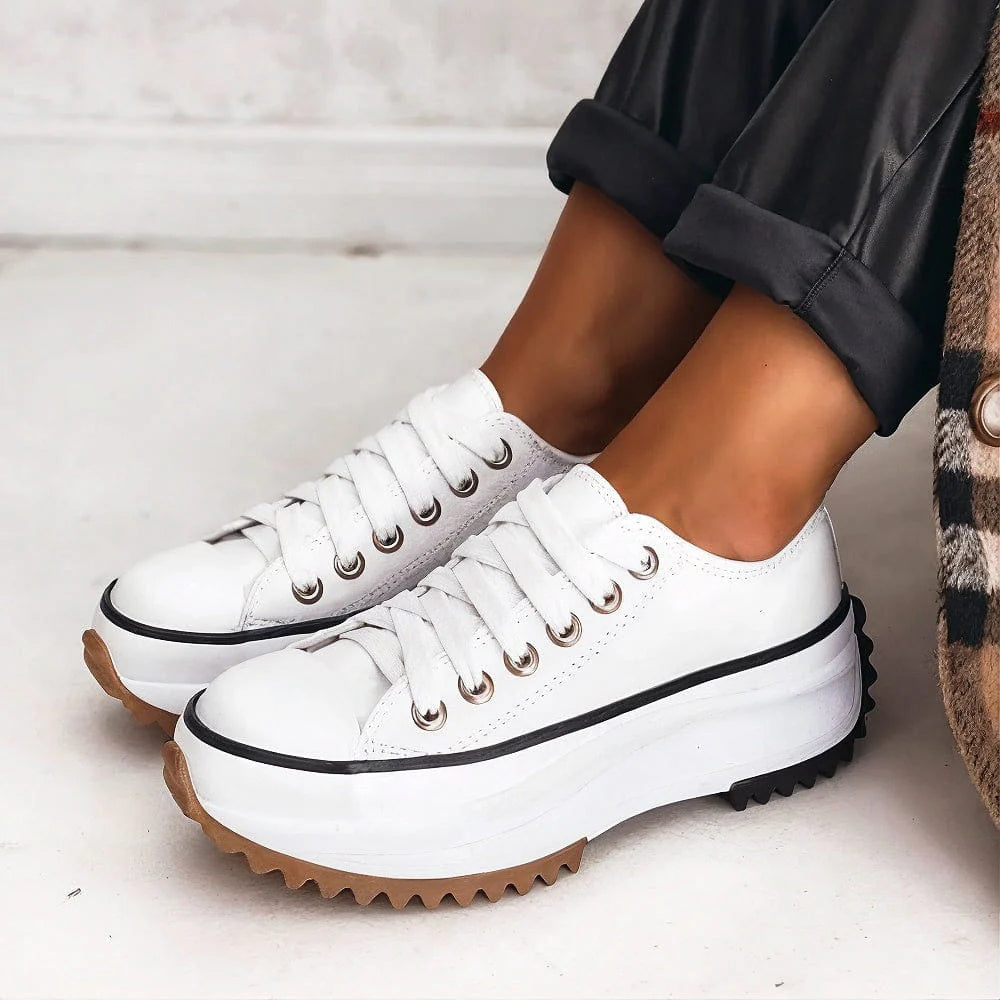 White sneakers with brown soles worn by a person on a light background