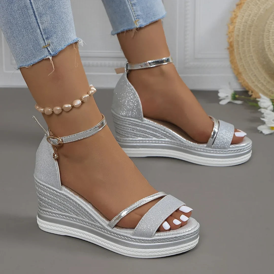 Silver glitter wedge sandals worn with light blue jeans on a neutral background