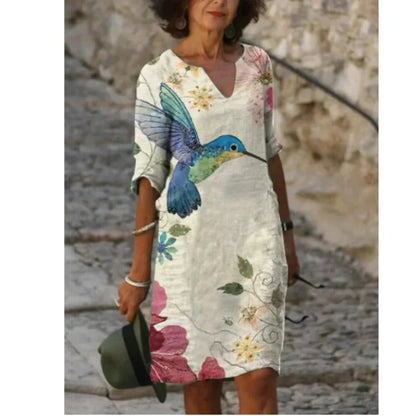 Woman wearing a floral dress with a colorful bird design, standing against a stone wall.
