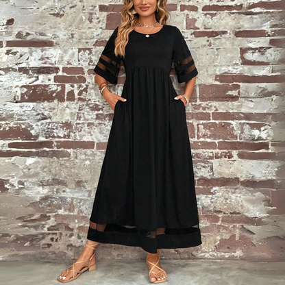 Woman wearing a black dress with sheer sleeves against a brick wall.