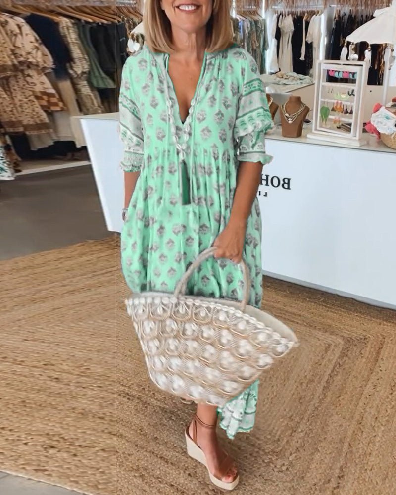 Woman wearing a green dress with a floral pattern, holding a clear handbag with pearls, standing in a clothing store.
