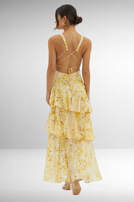 Woman wearing a yellow floral dress with a tiered skirt on a plain background