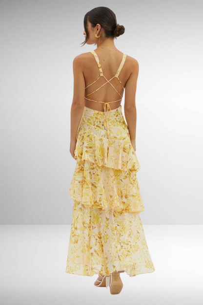 Woman wearing a yellow floral dress with a tiered skirt on a plain background