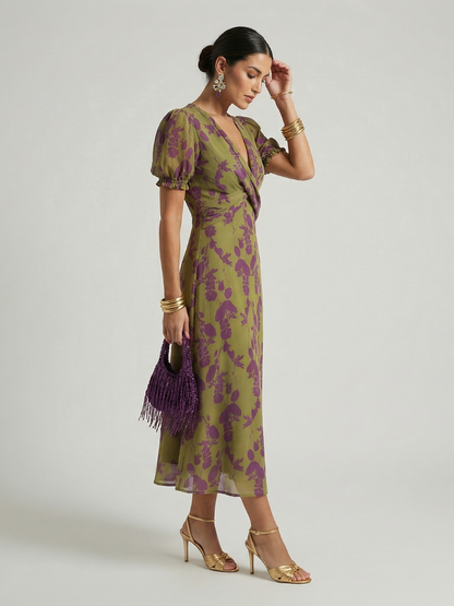 Woman wearing a green and purple floral dress with gold sandals on a light gray background