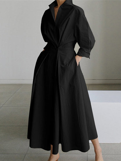 Person wearing a black dress with a tie waist in a minimalistic setting