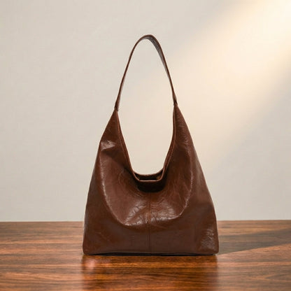 Dark brown leather shoulder handbag on a wooden surface with a neutral background