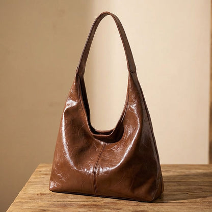 Dark brown leather vintage handbag on a wooden surface with a beige background
