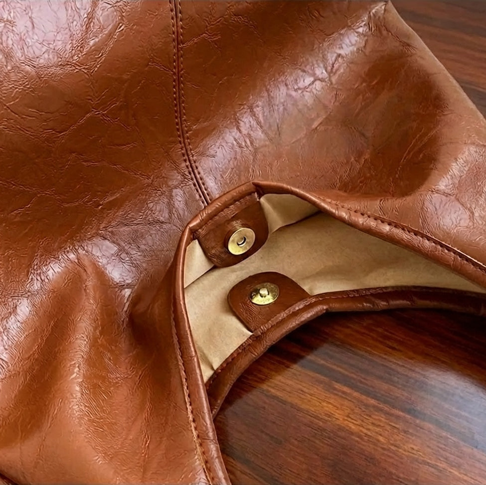 Close-up of a light brown leather shoulder purse with gold hardware on a wooden surface