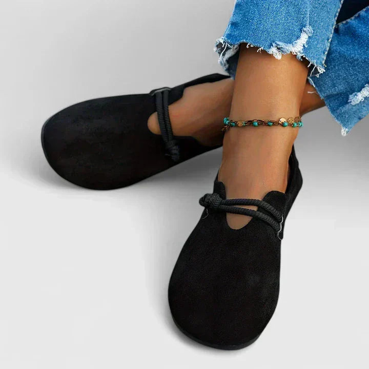 Black slip-on shoes worn with blue jeans on a light gray background