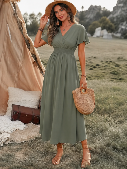 Woman in a green dress standing outdoors with a tent and suitcase in the background