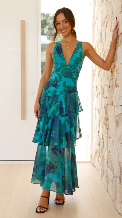 Woman wearing a blue floral dress standing against a stone wall.