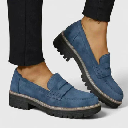 Blue loafers worn with black pants on a light gray background