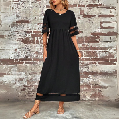 Woman wearing a black dress with sheer sleeves against a textured brick wall.