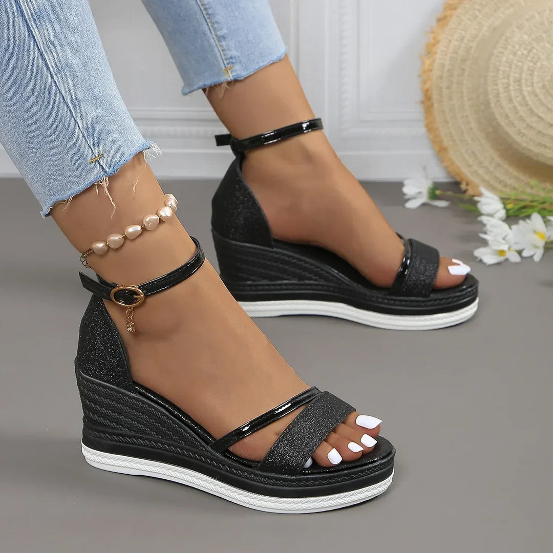 Black wedge sandals worn with light blue jeans on a neutral background