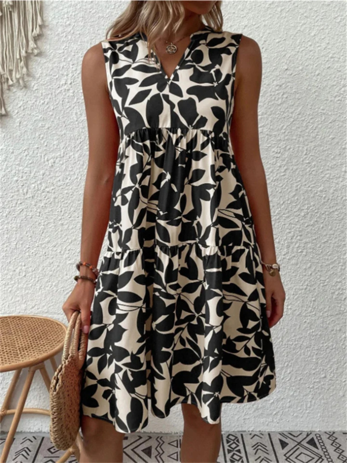 Woman wearing a black and white patterned dress against a white wall.