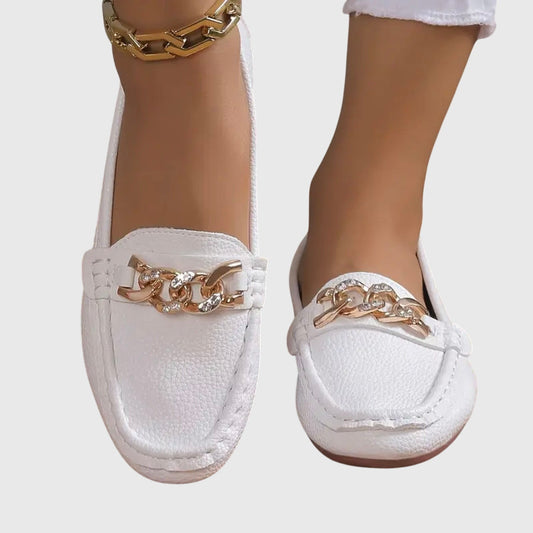 White loafers with gold chain details worn by a person on a light gray background