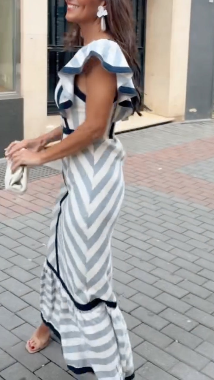 Woman wearing a gray and white striped dress with ruffled sleeves on a sidewalk.