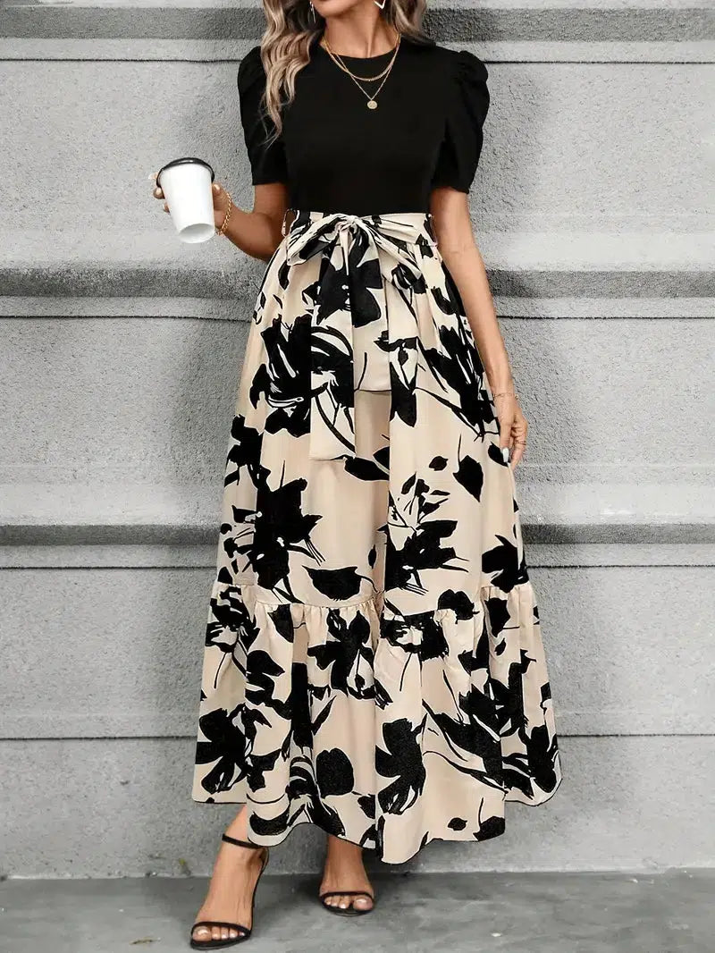 Woman wearing a black top and floral skirt against a gray wall.