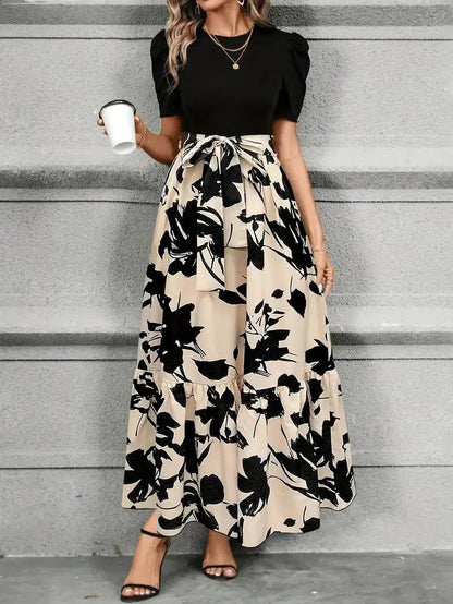 Woman wearing a black top and floral skirt against a gray wall.