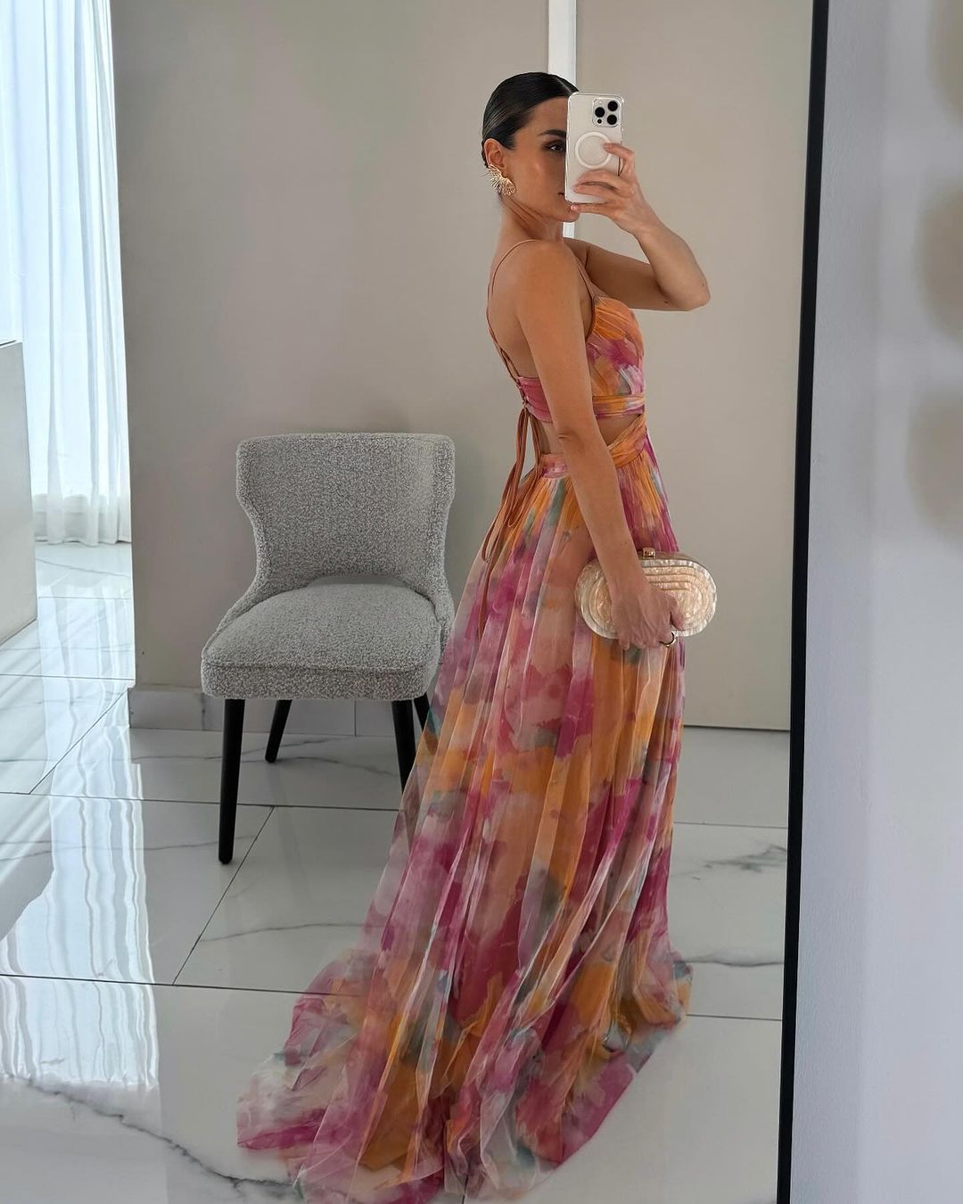 Woman in a colorful dress taking a mirror selfie in a modern room.