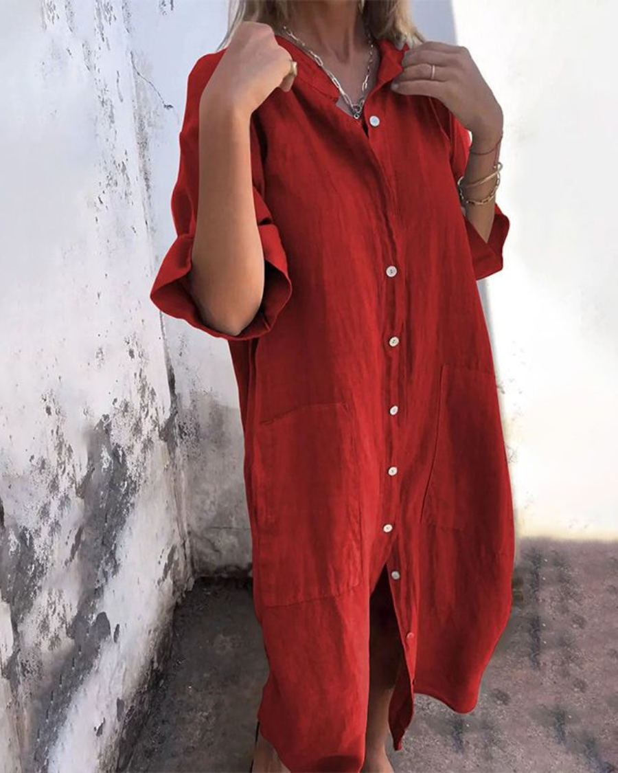 Person wearing a red dress with white buttons against a textured wall.