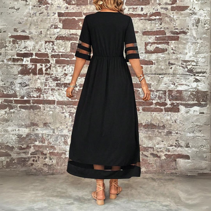 Person wearing a black dress with sheer sleeves against a brick wall.