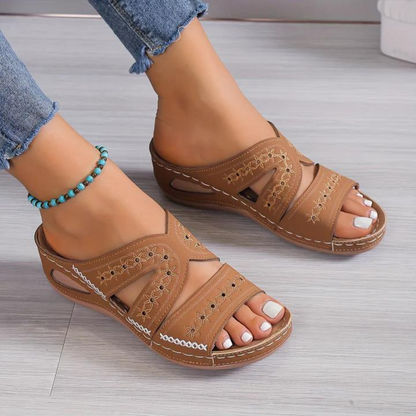 Brown sandals worn with denim jeans on a light wooden floor.