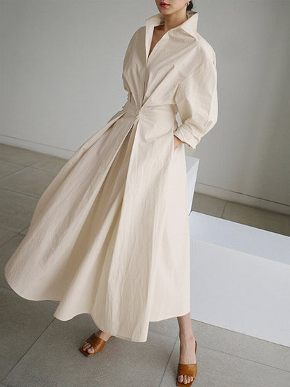Woman wearing a long beige dress with a belt in a minimalistic setting