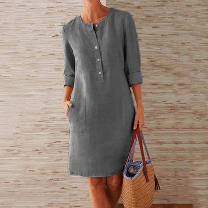 Woman wearing a gray dress holding a woven bag against a wooden panel background