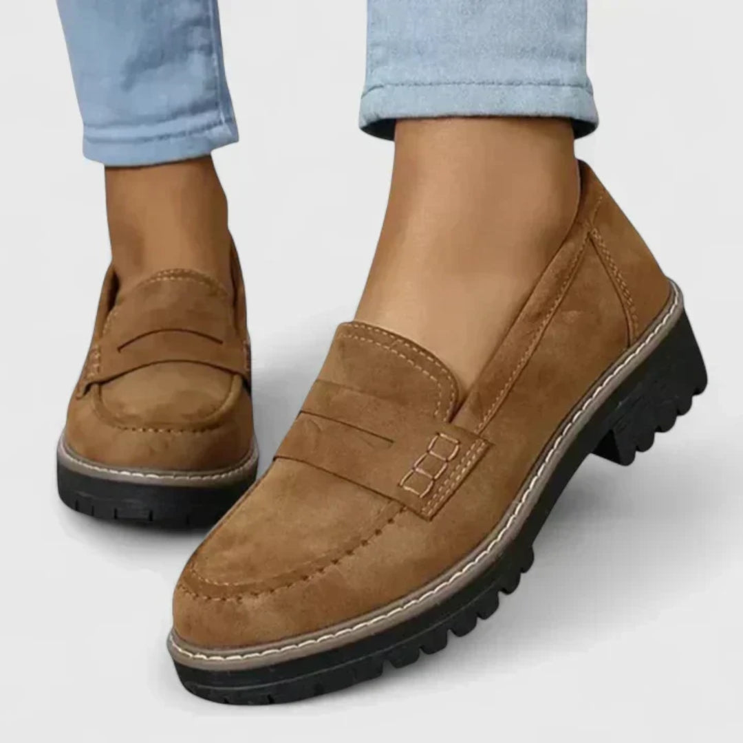 Brown loafers worn with light blue jeans on a white background