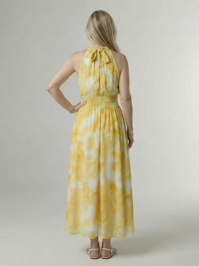 Woman wearing a yellow tie-dye dress against a plain background