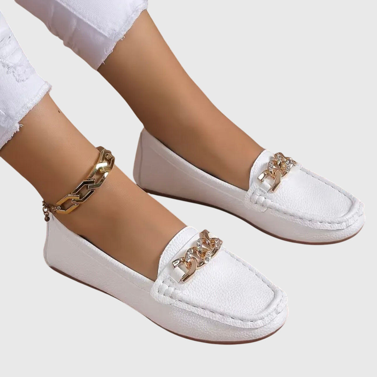 White loafers with gold accents worn by a person on a white background