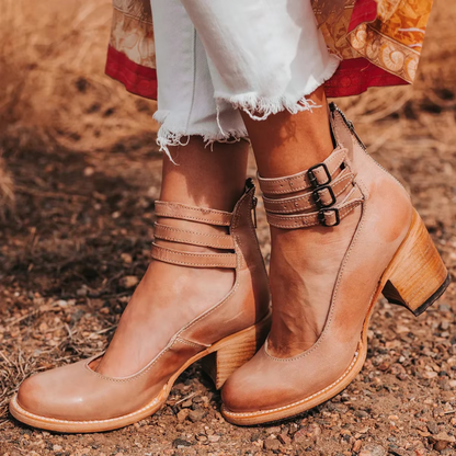 Tan leather ankle boots with buckles worn outdoors on a natural background
