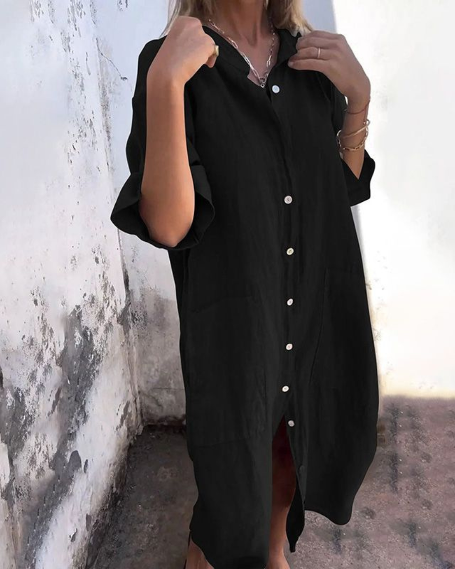 Person wearing a black button-up dress against a white wall.
