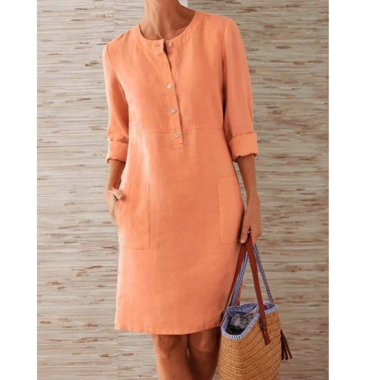 Person wearing an orange dress holding a woven bag against a wooden panel background
