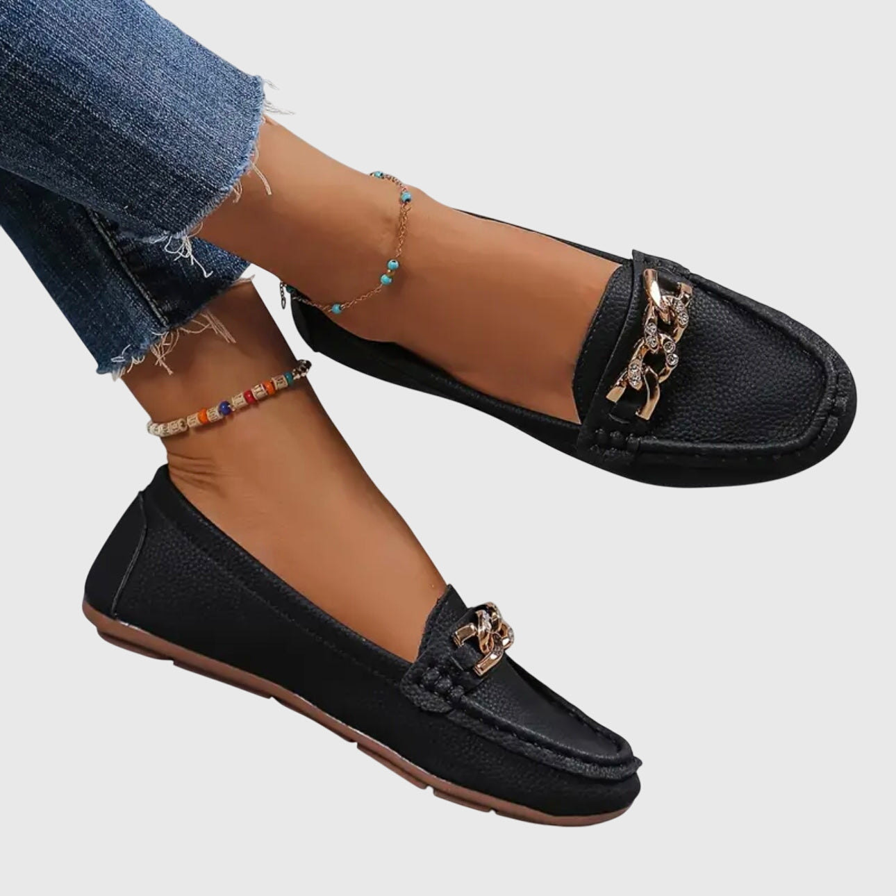 Black loafers with gold chain details worn by a person on a light gray background