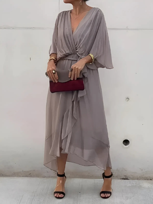 Woman wearing a gray dress with a red clutch against a white wall