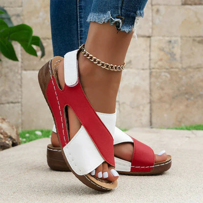 Red and white sandals worn with denim shorts against a stone wall background