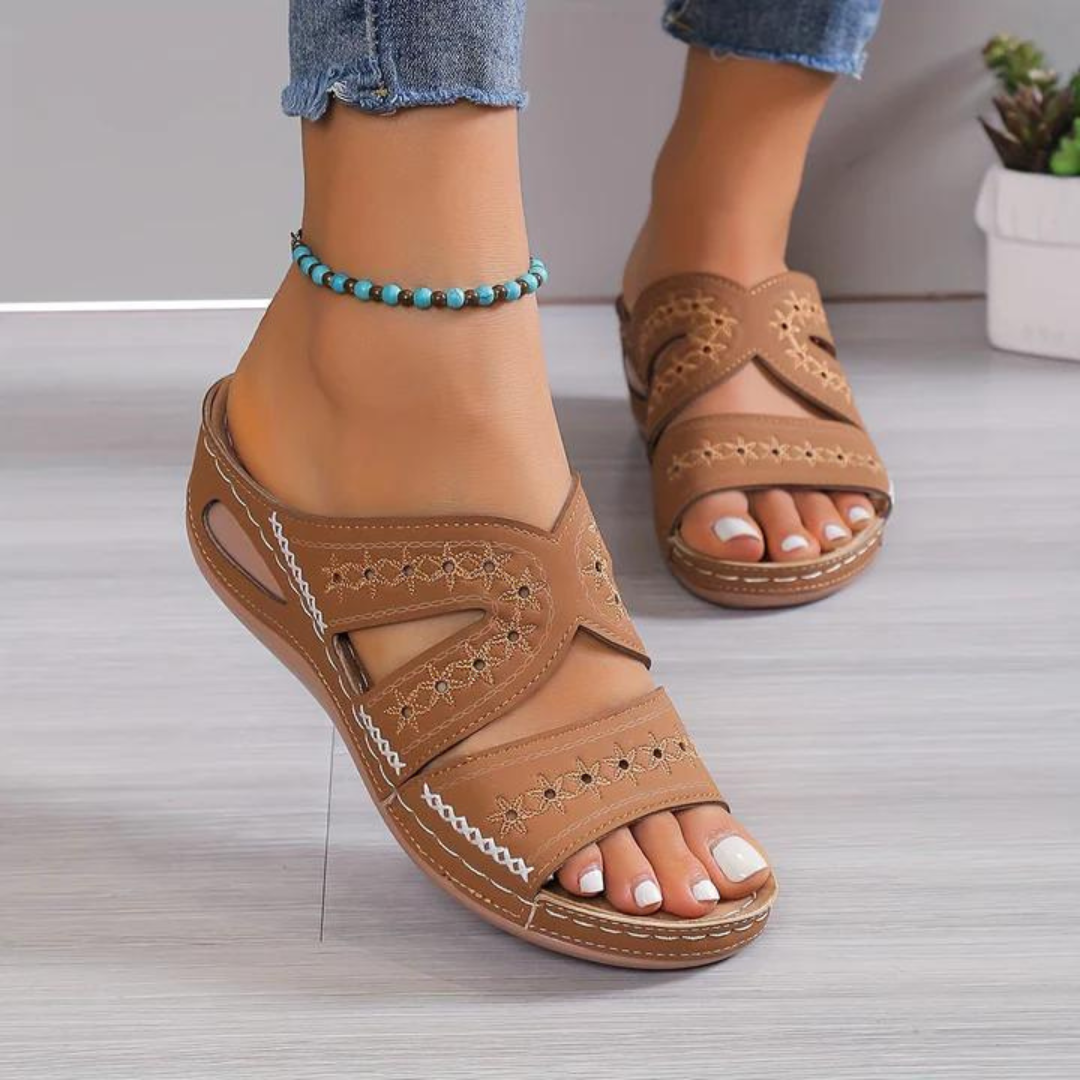 Brown sandals worn with blue jeans on a light wooden floor.