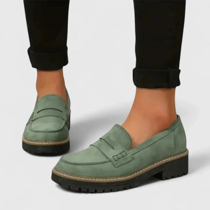 Green loafers worn with black pants on a light gray background