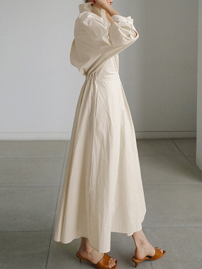 Person wearing a long beige dress in a minimalistic setting