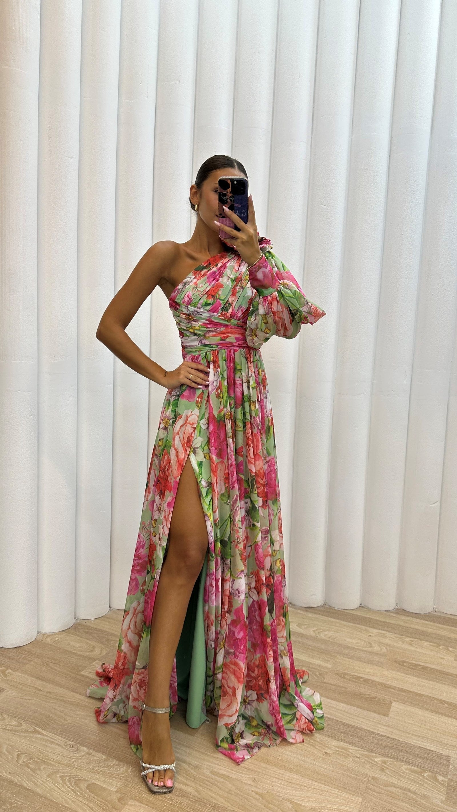 Woman in a colorful floral dress standing against white curtains.