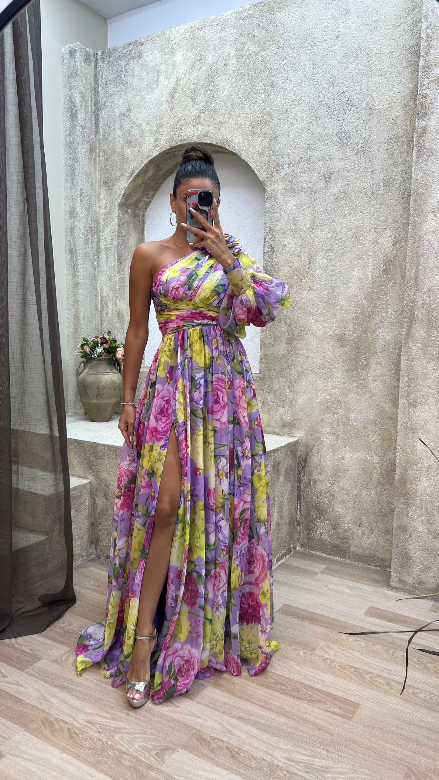 Woman in a colorful floral dress taking a mirror selfie in an outdoor setting.