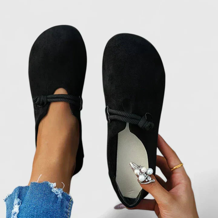 Black flats worn with denim jeans on a plain background