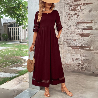 Woman wearing a burgundy dress with sheer sleeves against a brick wall.