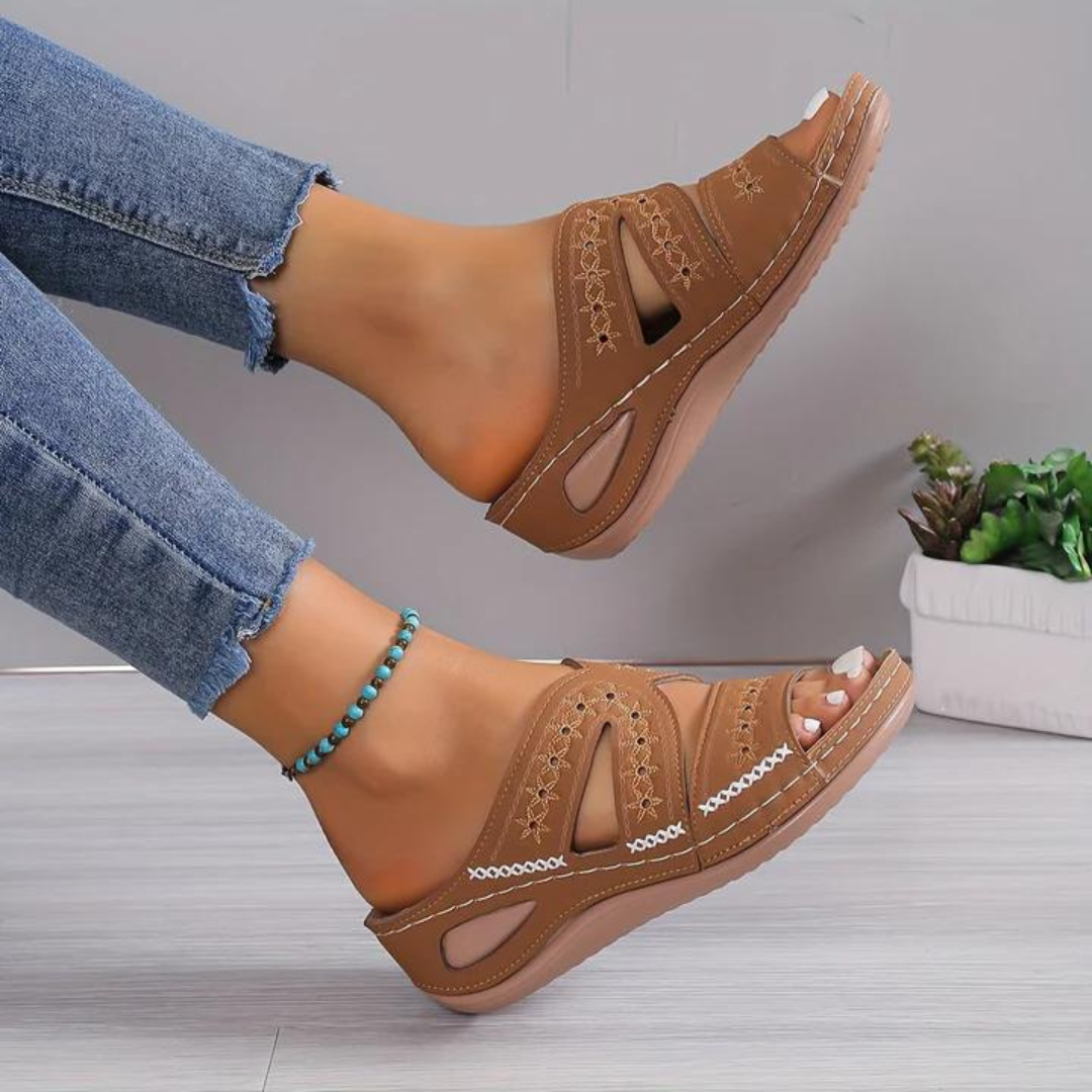 Brown sandals worn with blue jeans on a light gray background