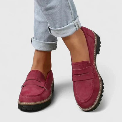 Red loafers worn with rolled-up jeans on a light gray background