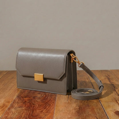 Gray leather handbag with gold accents on a wooden surface