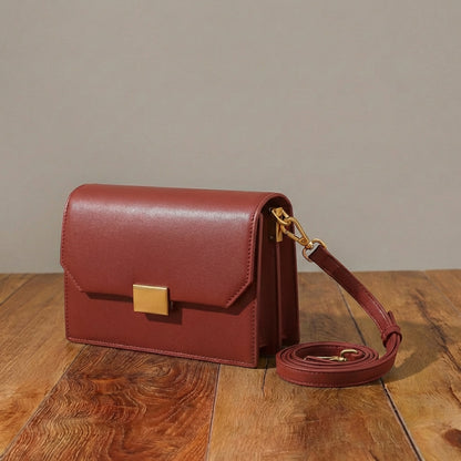 Red leather crossbody handbag with a gold clasp on a wooden surface