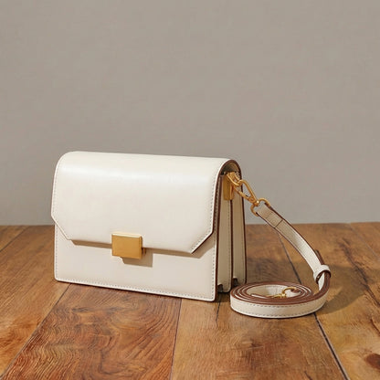 White crossbody bag with gold accents on a wooden surface